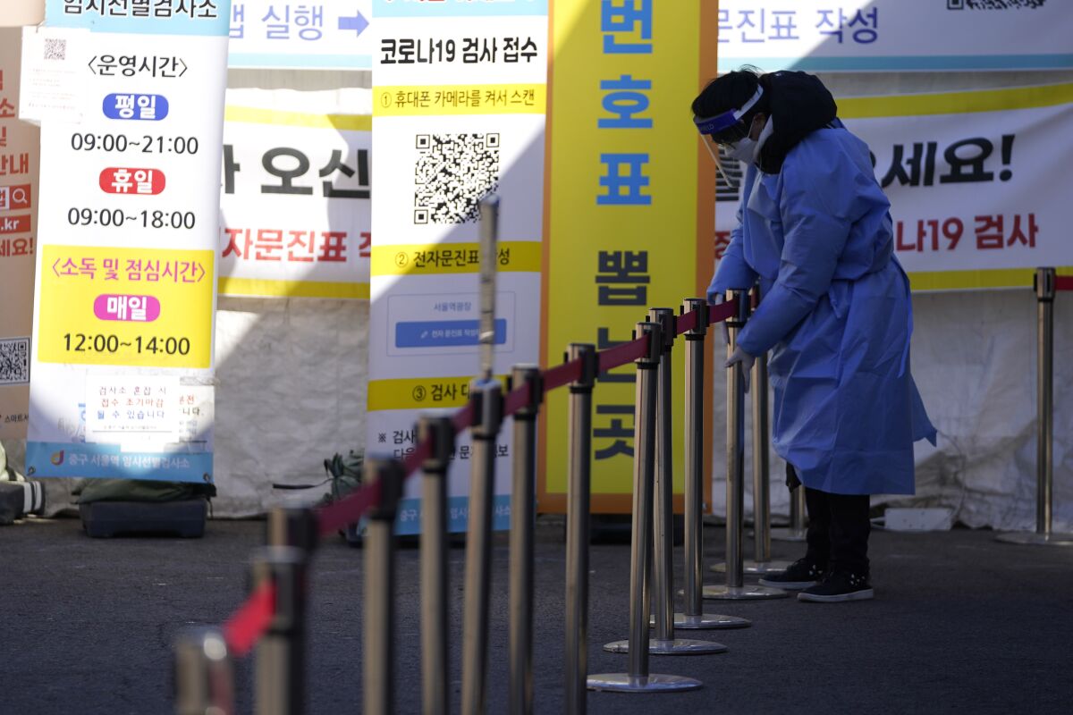 A health worker wearing protective gear sets up a barrier to accommodate a line of people 