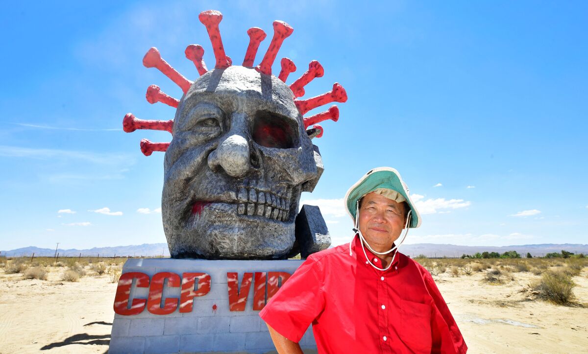 A man stands in a desert in front of a sculpture of a head.