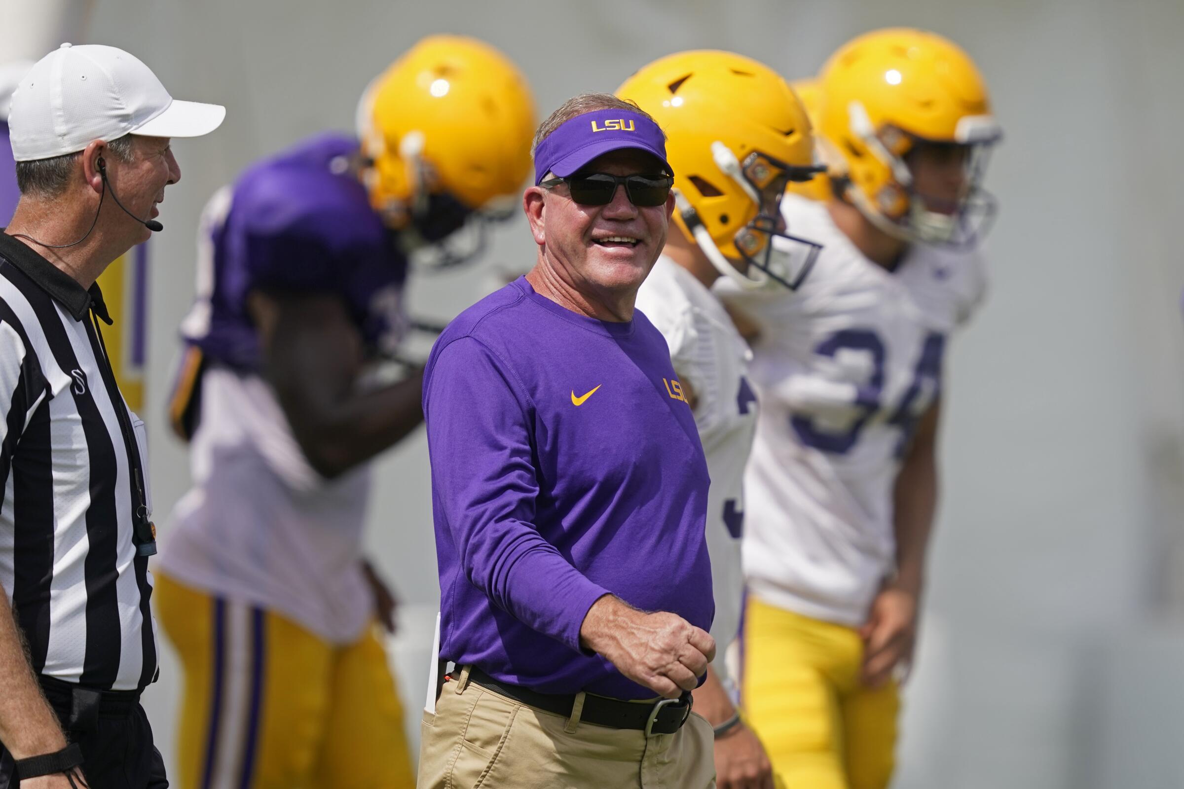 LSU head coach Brian Kelly smiles as he walks across the field during NCAA college football practice.