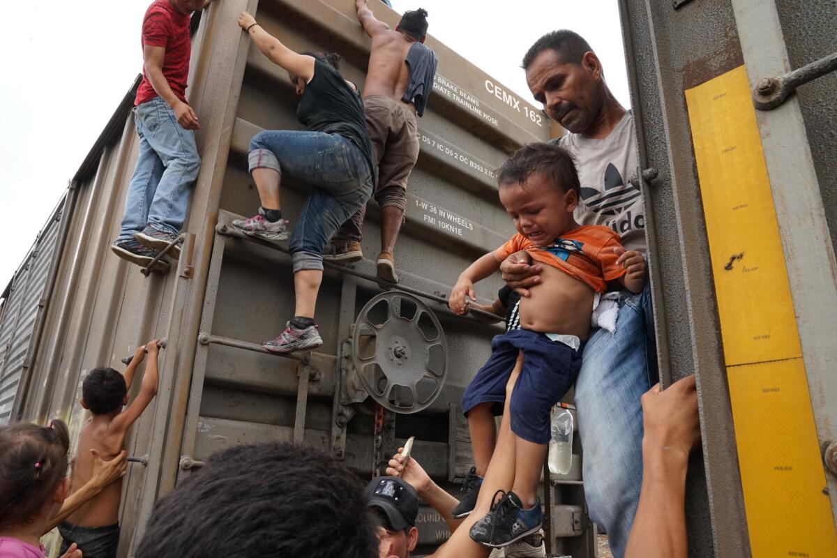 A crying child is handed up as migrants climb onto the roof of "La Bestia" for the trip across Mexico after the boxcars were locked to keep them from riding inside.