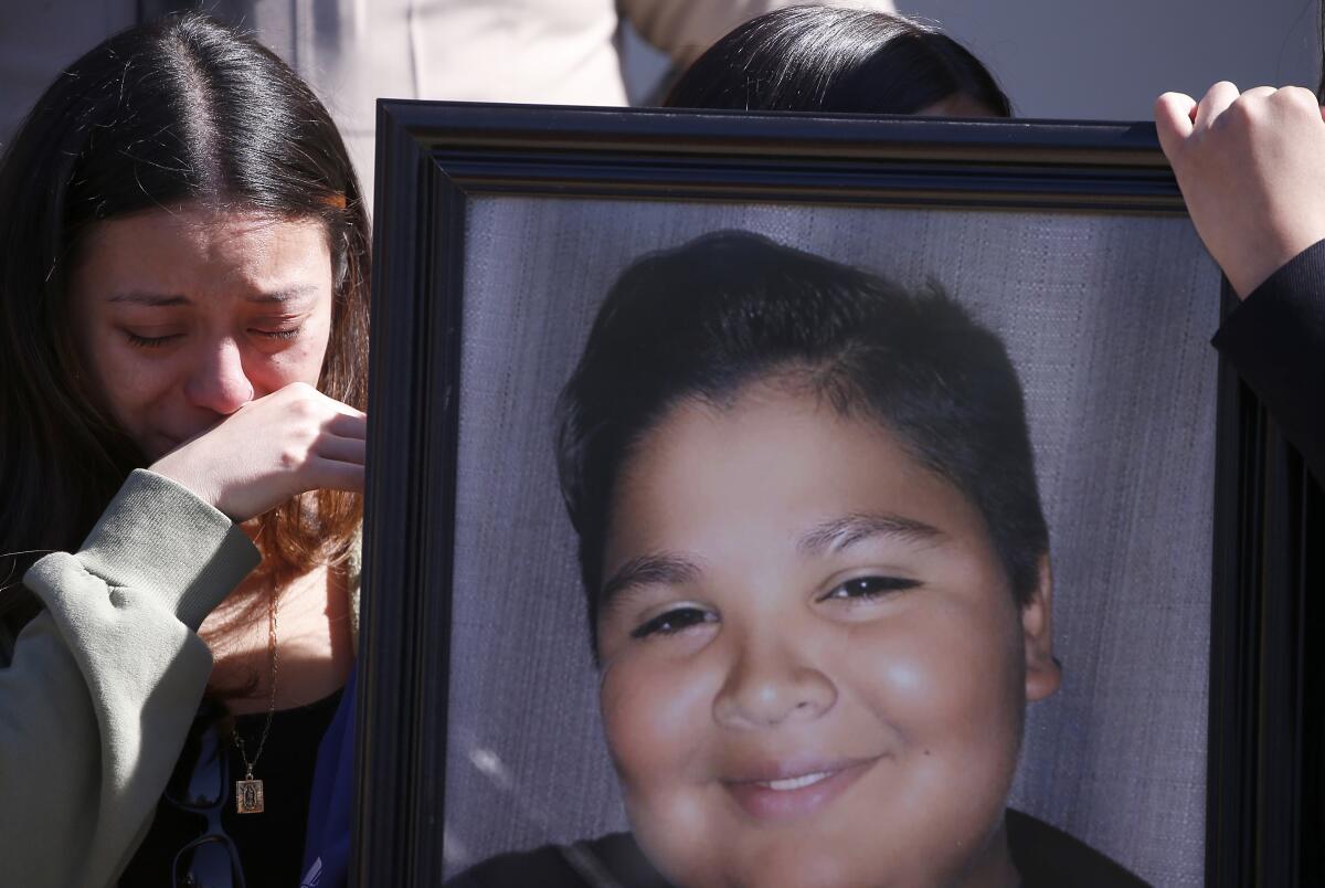 A young woman, crying, holds a photo of smiling boy.
