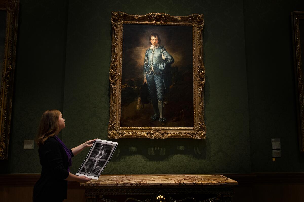 A paintings conservator looks up Gainsborough's "Blue Boy" while holding an X-ray of the artwork