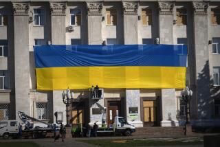 Municipal workers wearing protective vests and helmets decorate the wall of the regional administration building with a huge national flag to mark one year since the Ukrainian troops cleared the city from the Russian army, in Kherson, Ukraine, Friday, Nov. 10, 2023. (AP Photo/Efrem Lukatsky)
