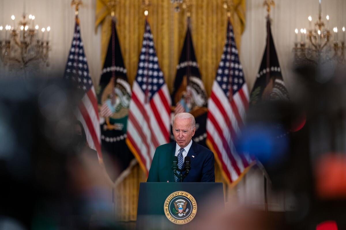 President Biden speaks at a lectern in front of a row of flags