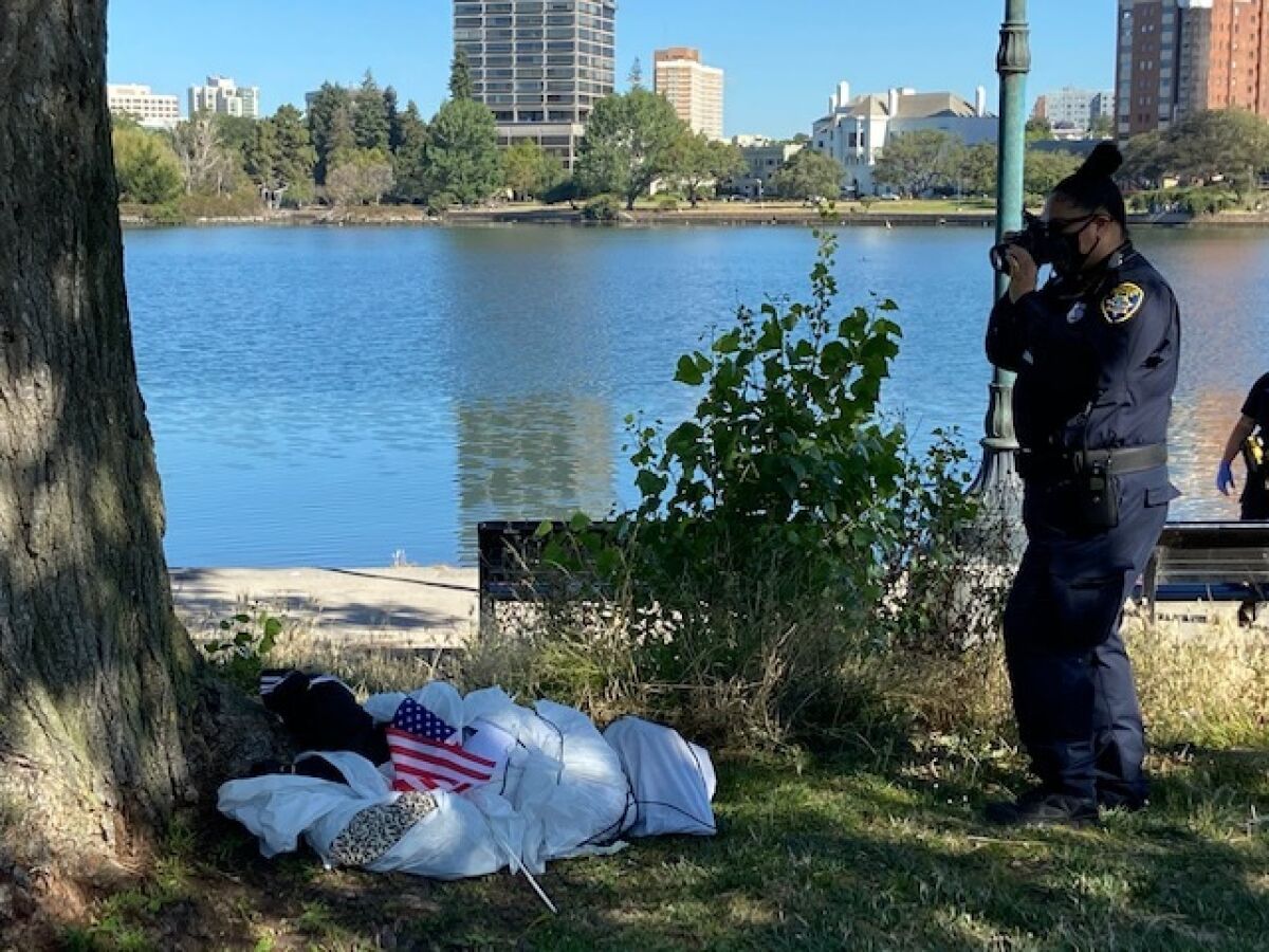 A police officer takes a photo of a figure that was hanging in effigy from a tree near Lake Merritt in Oakland