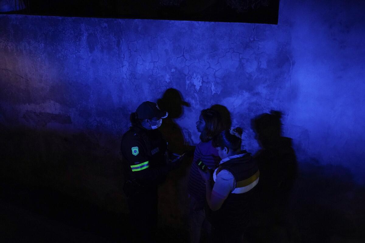 Police talk to a woman in dark blue lighting