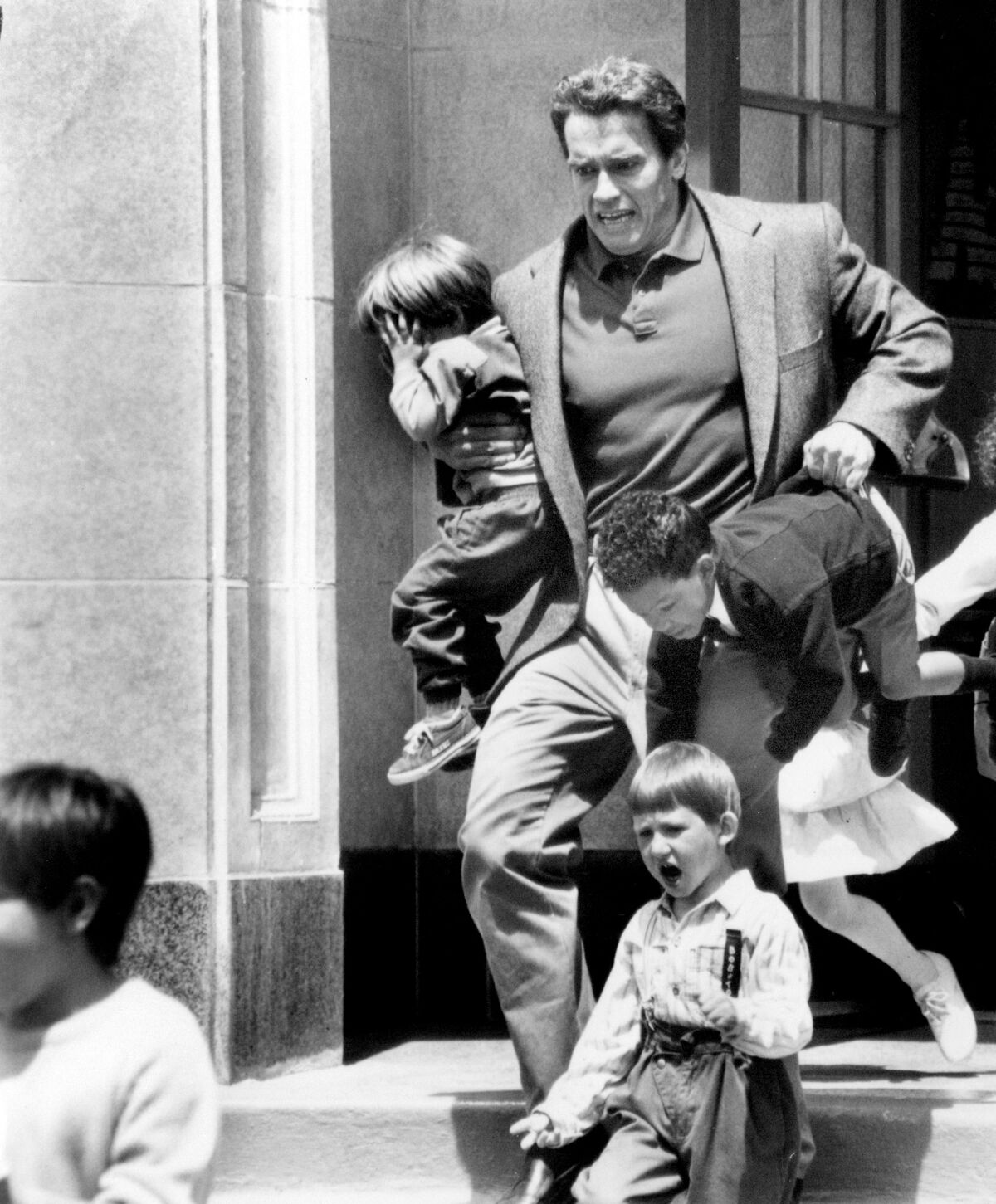 A man carries two small children down some steps.