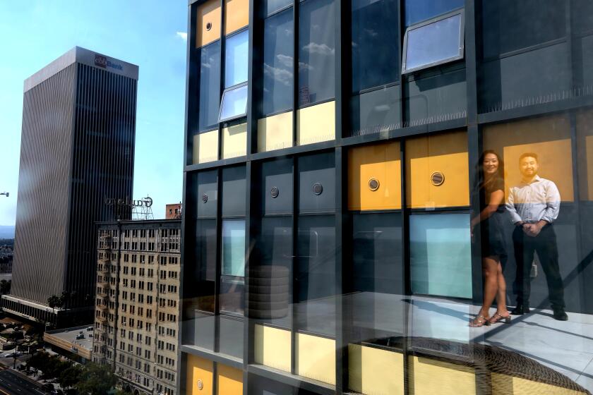 LOS ANGELES, CA - SEPTEMBER 7, 2022 - - Jaime Lee, left, chief executive of Jamison Realty Inc., and her brother Garrett Lee, president of Jamison Properties, are reflected in the facade of The Crosby apartments in Koreatown in Los Angeles on September 7, 2022. A growing number of Los Angeles-area office buildings are being converted to residential use as demand for offices stalls. Many of L.A.'s early 20th century office buildings were converted to residential use years ago, but now there is a move to convert mid-century properties as demand for housing surpasses demand for offices in key neighborhoods. Some of the amenities are a pool on the roof, a dog park, a community space to do business, a gym and a room for karaoke singing. (Genaro Molina / Los Angeles Times)