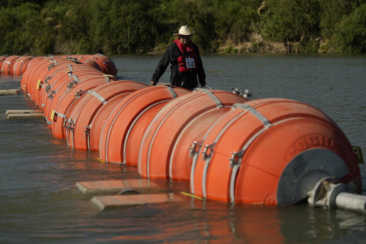 A person appears next to a line of big orange buoys in water.