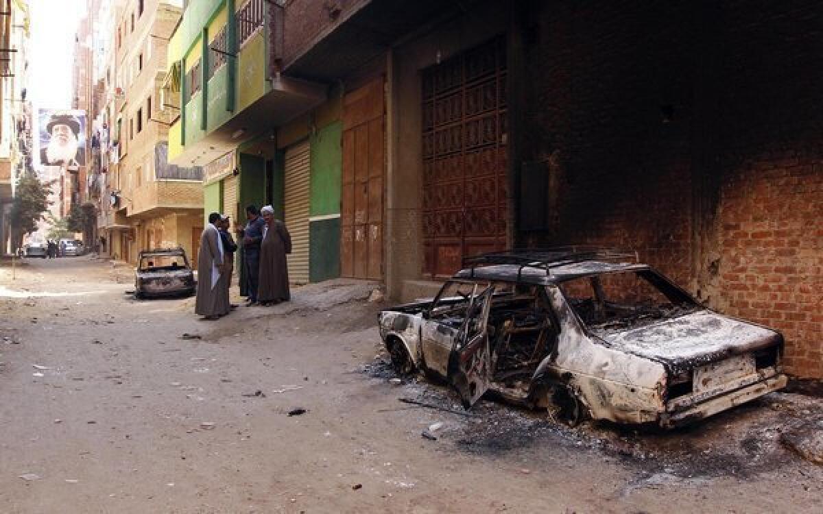 Several burned cars belonging to Egyptian Christians remain in the street after clashes between Muslims and Christians just outside Cairo on Saturday. A picture of the late Coptic Pope Shenouda is seen at end of street.