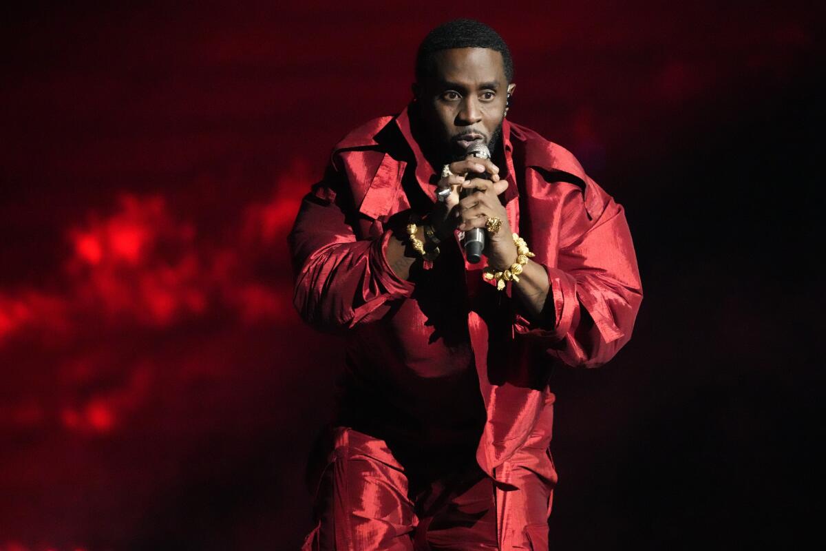 Sean "Diddy" Combs wears a shiny red puffer jacket and matching pants while holding a microphone onstage with both hands.