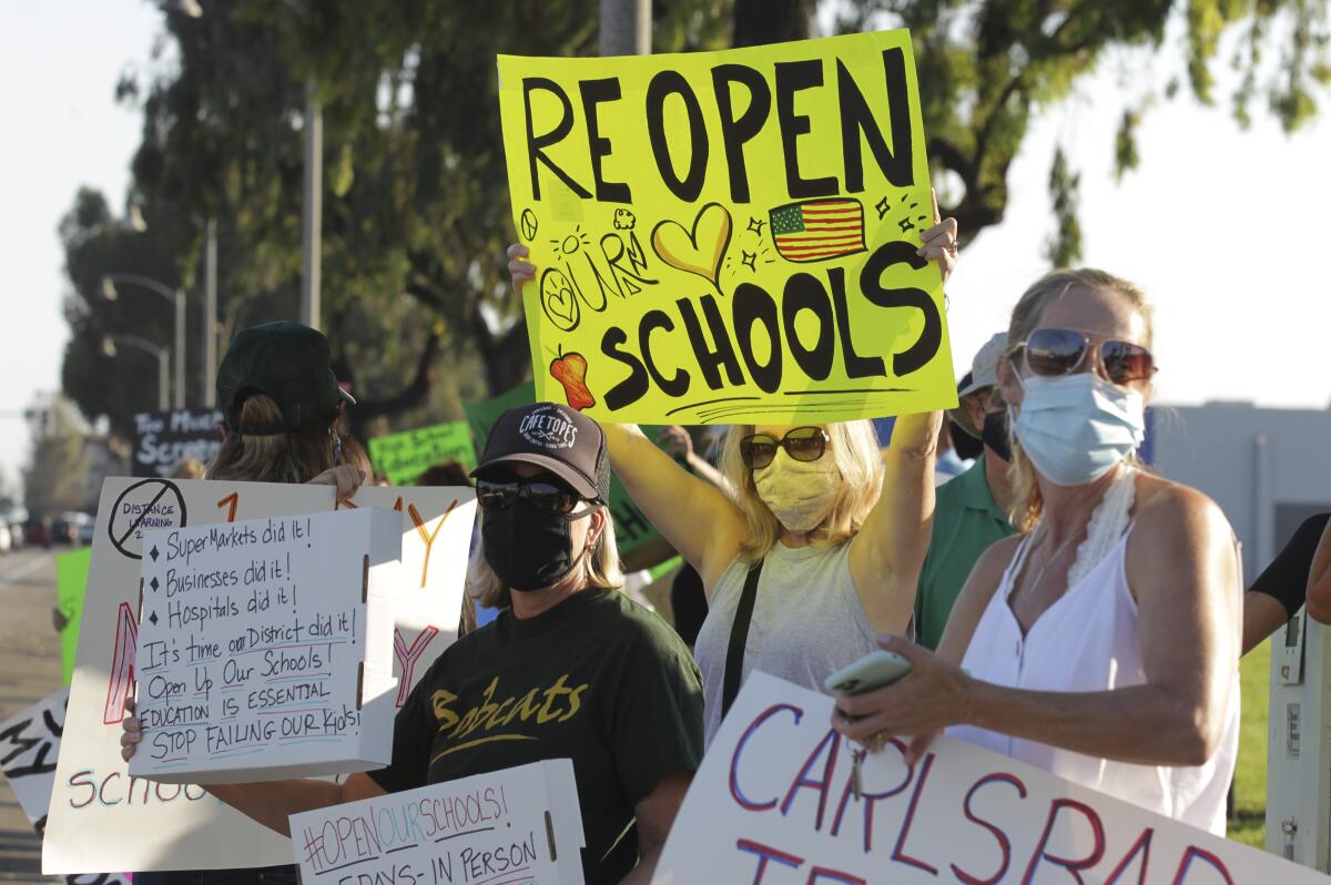 Parents hold signs for schools to reopen at a protest last September at the Carlsbad School district headquarters.