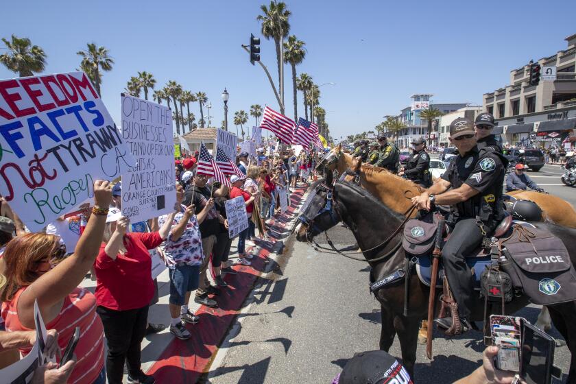 HUNTINGTON BEACH, CA -- FRIDAY, MAY 1, 2020: Mounted police line up to keep protesters on the sidewalk as thousands of protesters rally at the intersection of Main Street and Pacific Coast Highway in the``March to Open California'' to call on Gov. Newsom to relax the state's stay-at-home orders under COVID-19 in Huntington Beach, CA, on May 1, 2020. (Allen J. Schaben / Los Angeles Times)