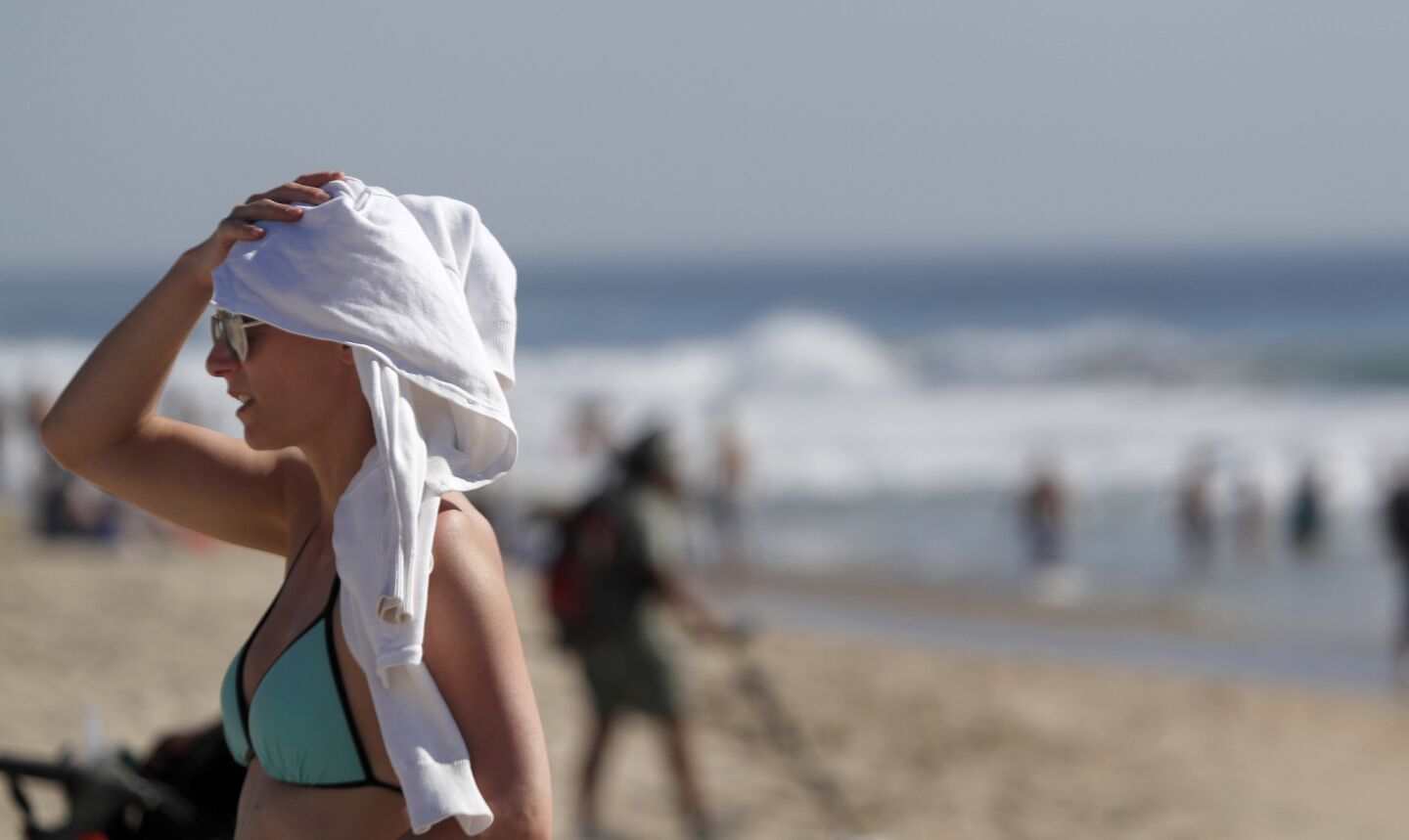 A woman uses a towel for shade while relaxing at the Huntington Beach Pier.