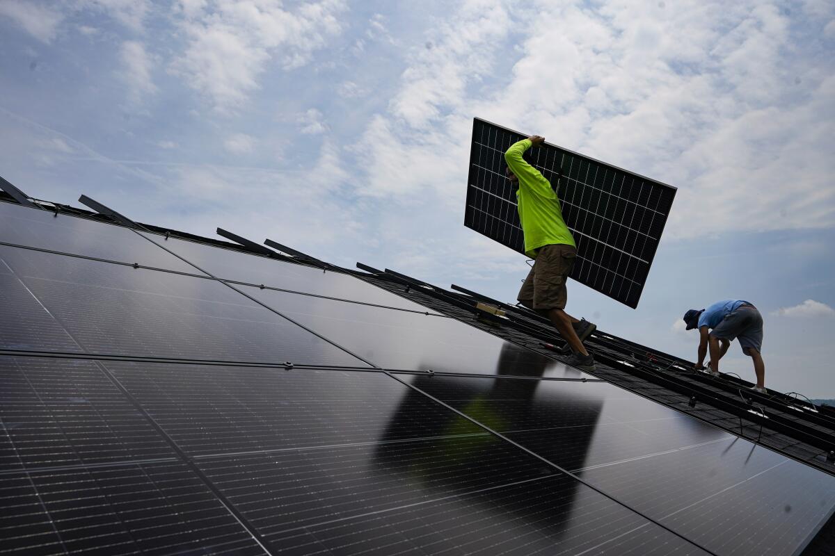 Nicholas Hartnett carries a panel as he and Brian Hoeppner install a solar array on the roof of a home.
