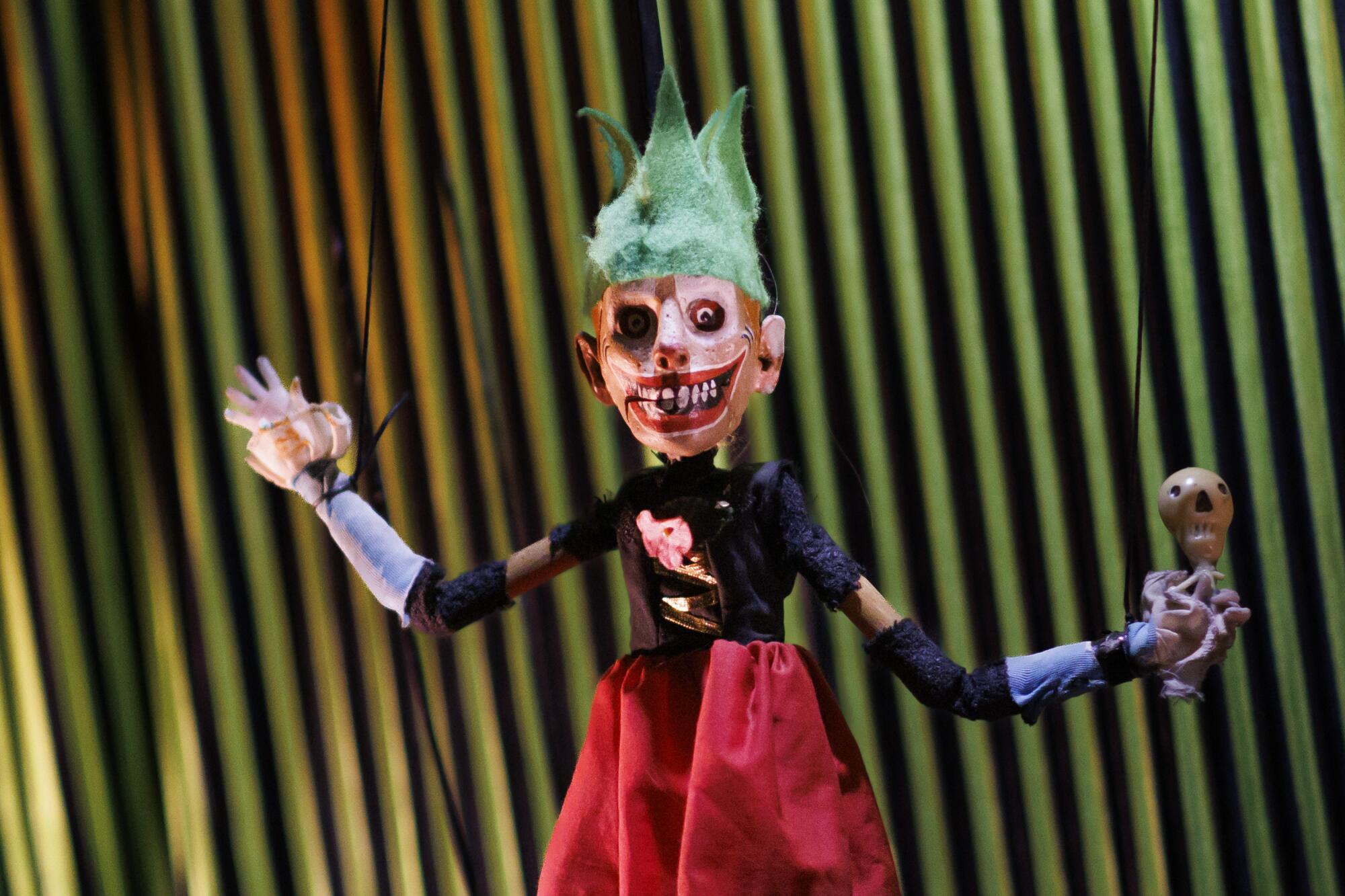 A marionette on a stage wearing a red dirndl and green felt crown.
