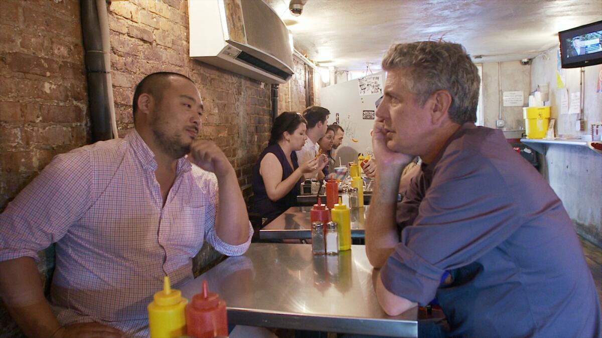 Two men sit across from each other at a metal table with ketchup and mustard dispensers on it.