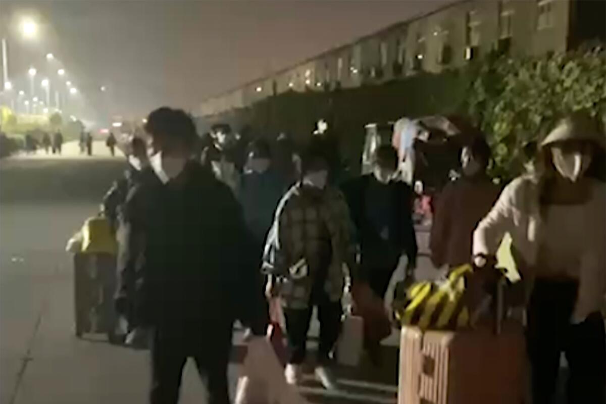 People wearing masks and carrying suitcases and bags leave a Foxconn compound at night.