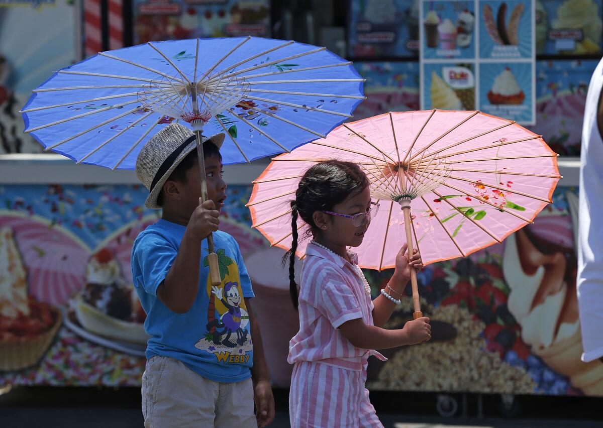 Michael and Maya Gutierrez walk with umbrellas for shade Friday during opening day of the Orange County Fair in Costa Mesa.