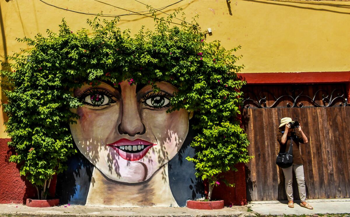 A tourist stands beneath a mural in San Miguel de Allende, Mexico.