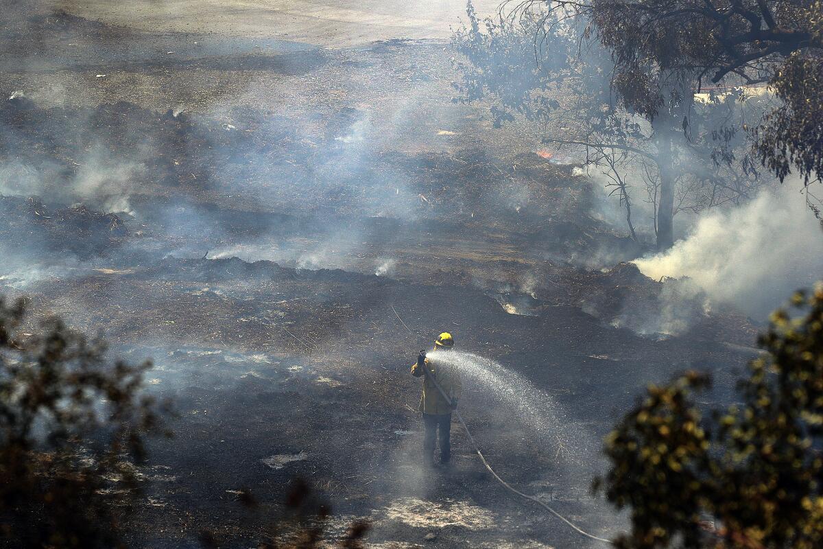 A firefighter points a hose at a hot spot in a grassy area between the 134 and 2 freeways as fire crews from Glendale and Los Angeles continue to battle a brush fire that erupted in Eagle Rock on Sunday.