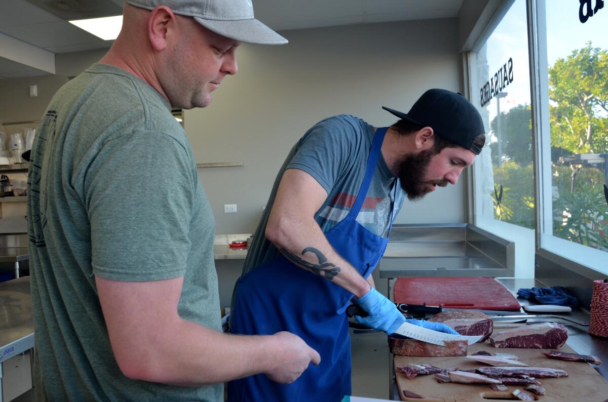 Ryan Ramming looks on as butcher James Croix trims dry-aged New York strip steak.