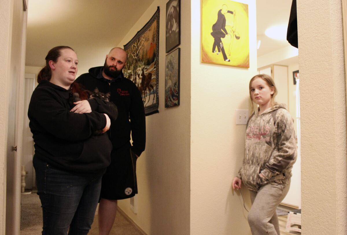 A woman holding a cat, a man and a girl stand in the hallway of their home.