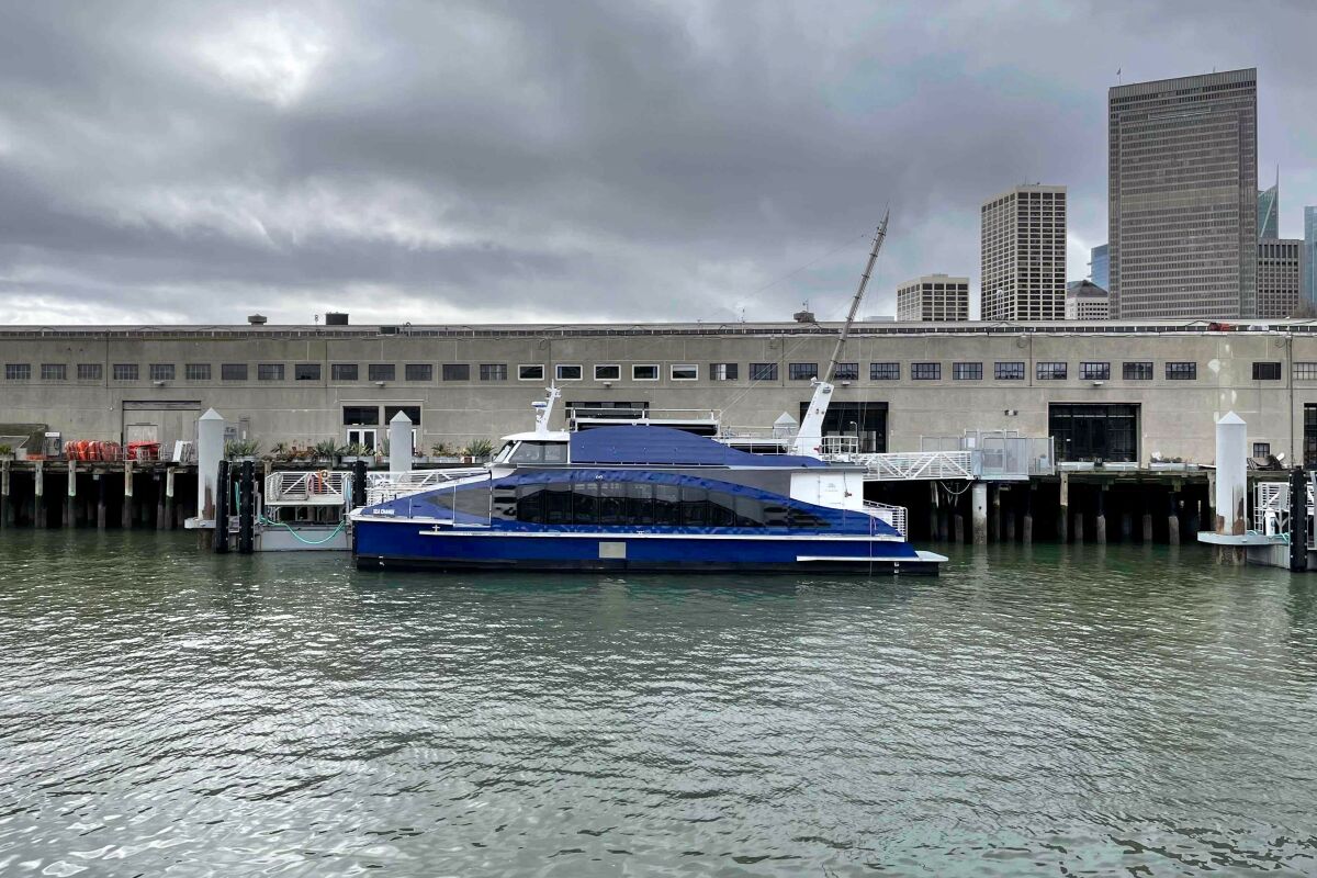 A dark blue boat docks at a pier. High-rises are seen in the background.