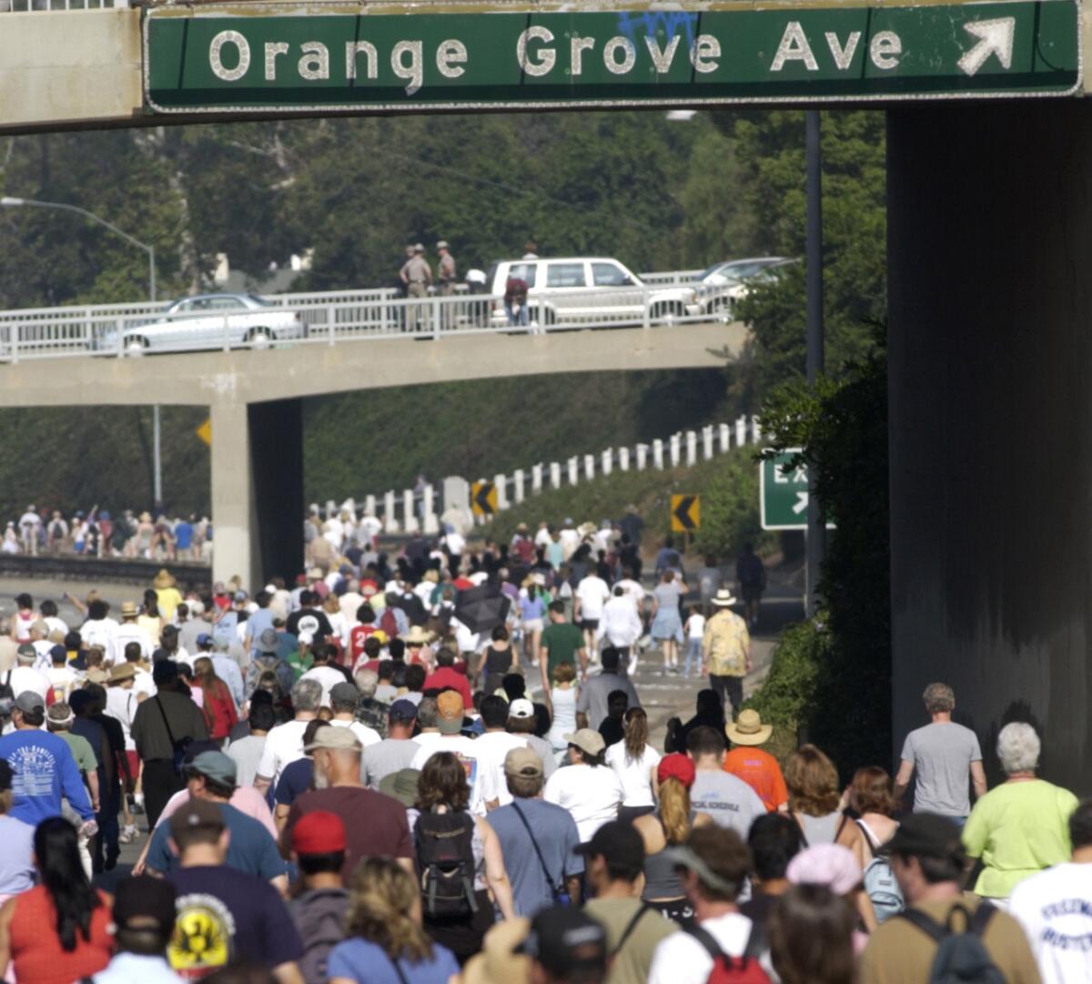 A large crowd of people walking on a freeway under a sign for Orange Grove Avenue exit