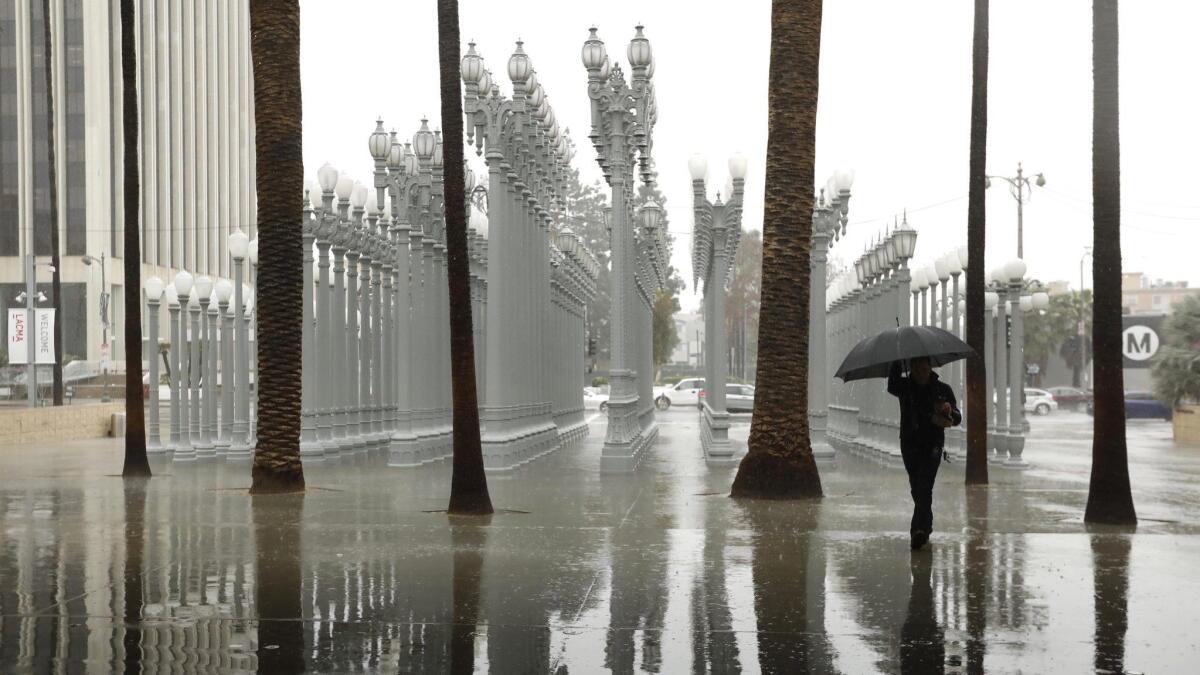 More rain is likely to hit Los Angeles on Wednesday. Here, a visitor to the Los Angeles County Museum of Art makes his way through the rain near Chris Burden’s sculpture “Urban Light” during a Feb. 14 storm.