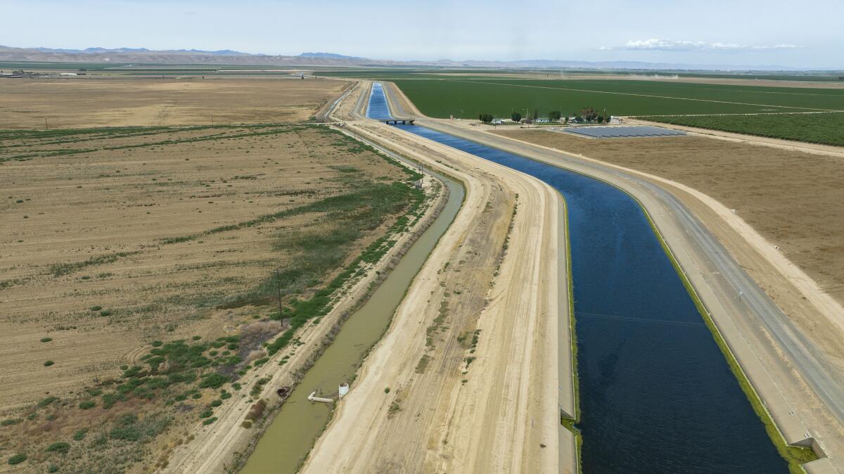 A canal carves cuts through flat farmland.  