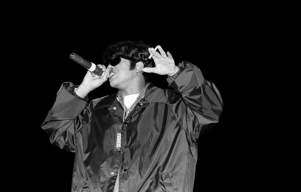 Boss wears an oversize windbreaker while rapping into a handheld microphone onstage with her other hand in the air