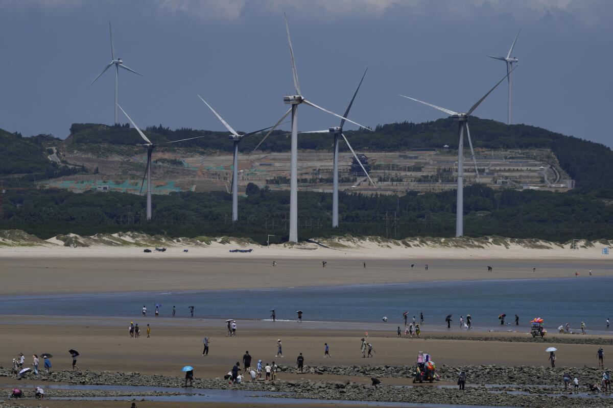 Beachgoers walk near wind turbines along the coast of Pingtan in Southern China's Fujian province, on Aug. 6, 2022. The world's two biggest emitters of greenhouse gases are sparring on Twitter over climate policy, with China asking if the U.S. can deliver on the landmark climate legislation signed into law by President Joe Biden this week. (AP Photo/Ng Han Guan)
