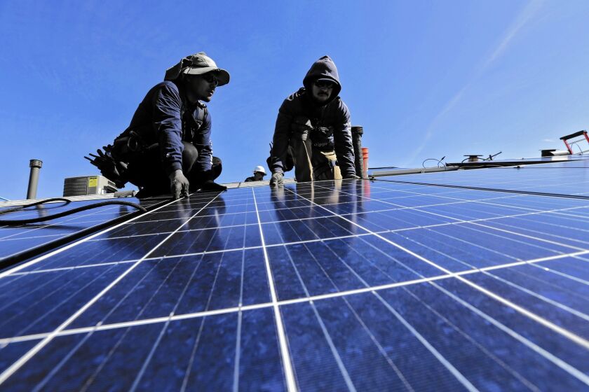 Workers install a rooftop solar system on a Van Nuys home. Clean energy advocates say policies for addressing climate change can help create jobs.