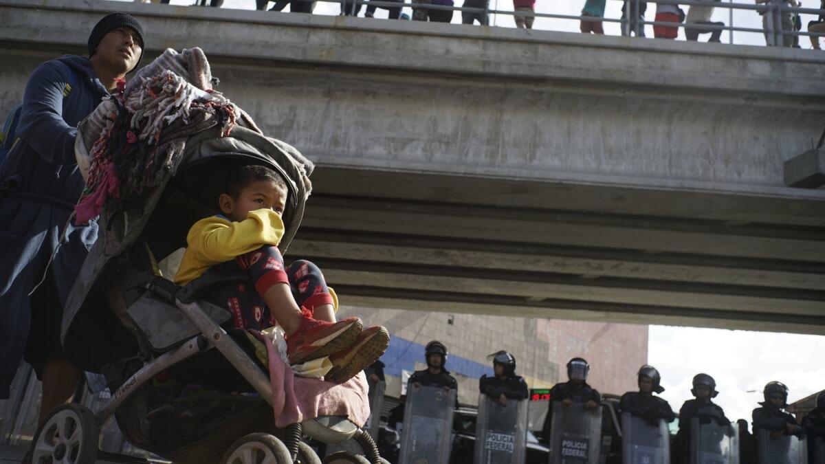 A migrant pushes a child in a baby stroller past a cordon of riot police as he joins a small group trying to cross the border in Tijuana, Mexico.