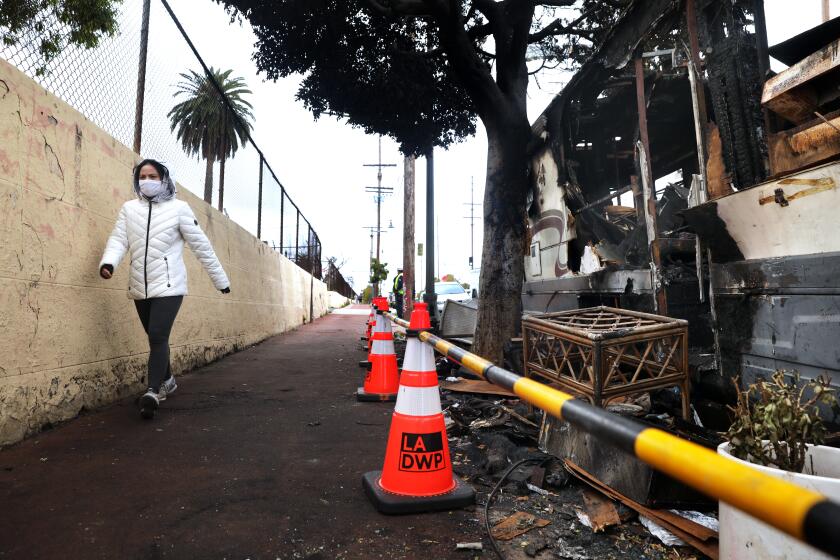 LOS ANGELES-CA-APRIL 3, 2023: A pedestrian walks past a burned RV parked along the Evergreen Jogging Path in Boyle Heights on April 3, 2023. (Christina House / Los Angeles Times)