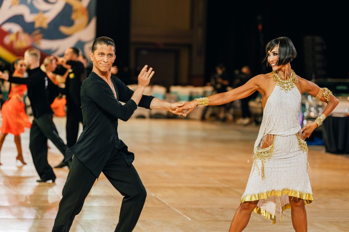 A Pro-Am dance team on the dance floor: a man all in black and a woman in a white dress.