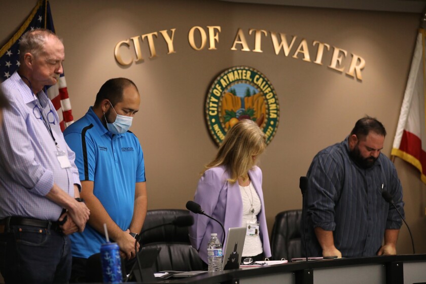 ATWATER, CA - MAY 26, 2020 - - Atwater City Council members John Cale, from left, Danny Ambriz, City Manager Lori Waterman, and Mayor Pro Tem and City Council member Brian Raymond bow their heads during the invocation at the start of a city council meeting in Atwater on May 26, 2020. The city of Atwater in Merced County has declared itself a "sanctuary city" from the state's stay-at-home orders and has been open for business for over a week now. (Genaro Molina / Los Angeles Times)
