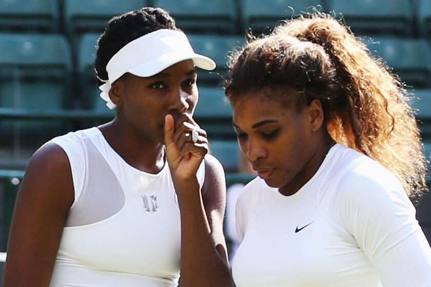 Venus, left, and Serena Williams look on during their doubles match at Wimbledon on Tuesday. Serena Williams defaulted out of the match when she couldn't hit a serve fast enough to register on the speed gun.