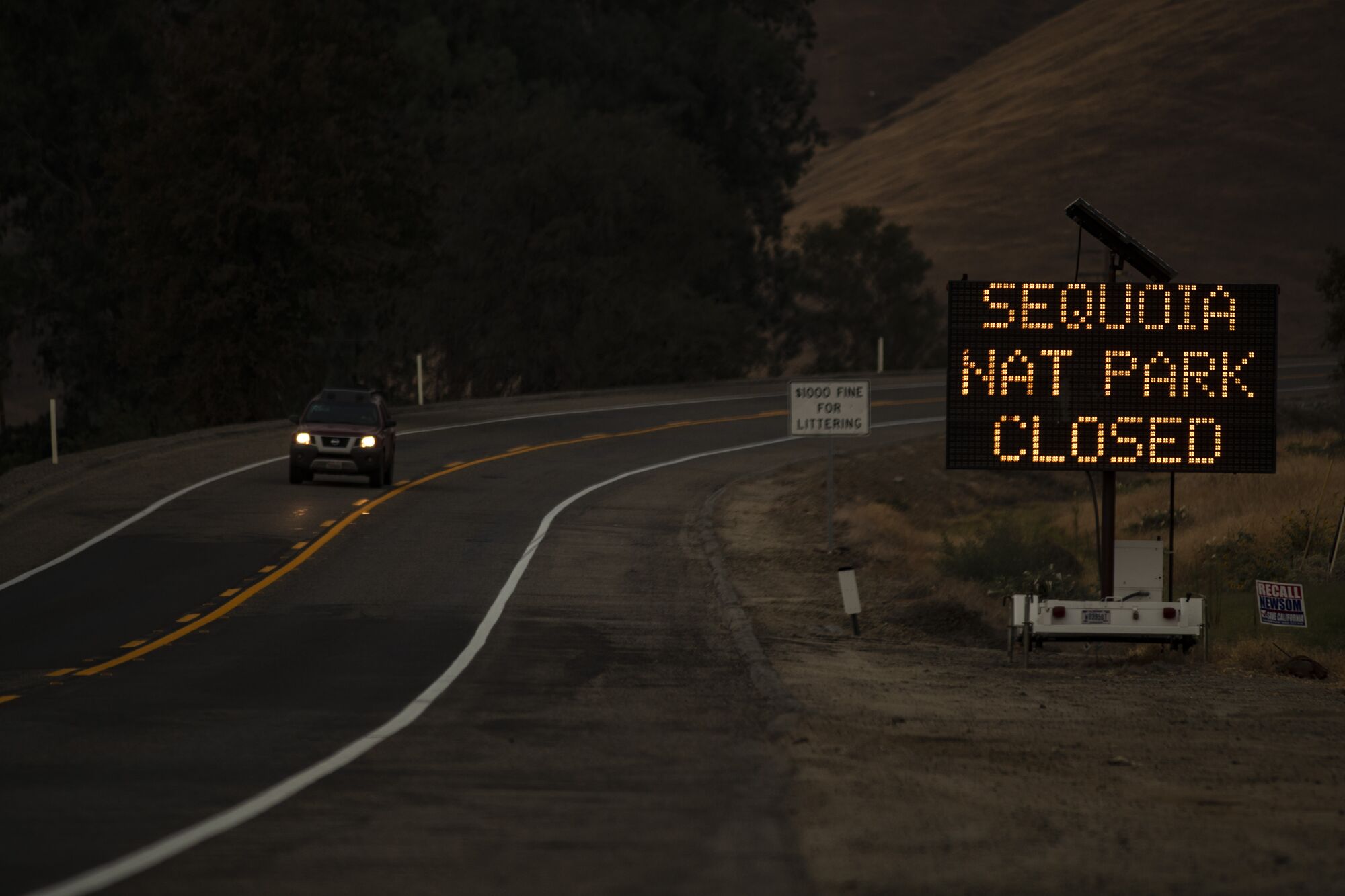 A car with headlights on drives away from a message sign announcing the closure of Sequoia National Park