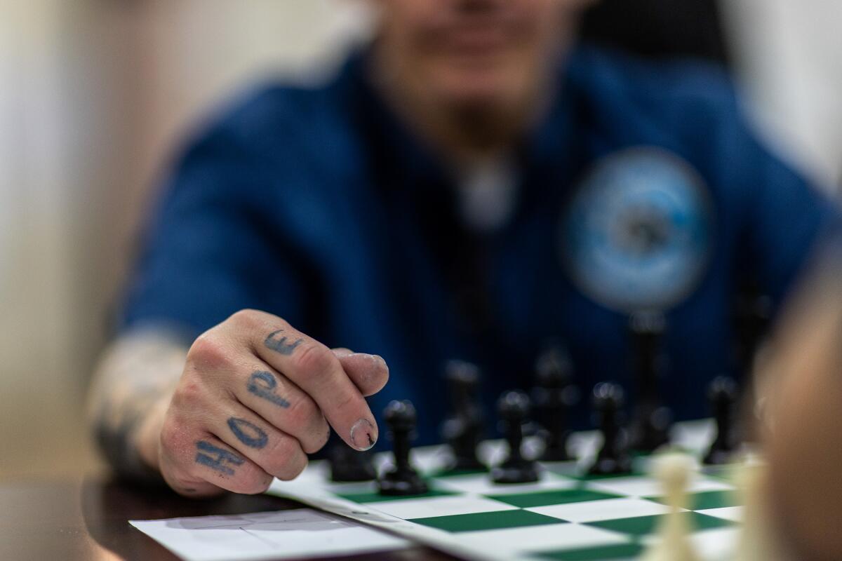 An inmate with "HOPE" tattooed on his knuckles plays chess.