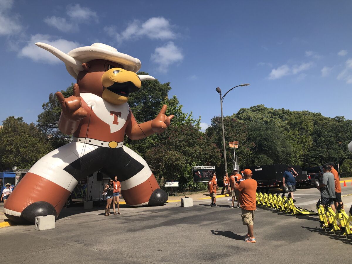A man takes a picture of two people in front of a giant inflatable Longhorn on the street