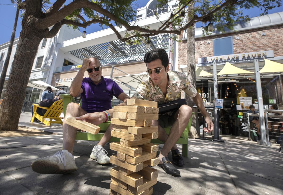 Two people play giant Jenga outside an area with restaurants