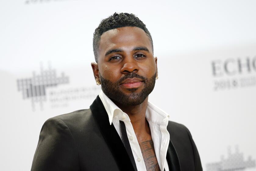 Jason Derulo in an unbuttoned suit shirt and a black blazer posing in front of a white background