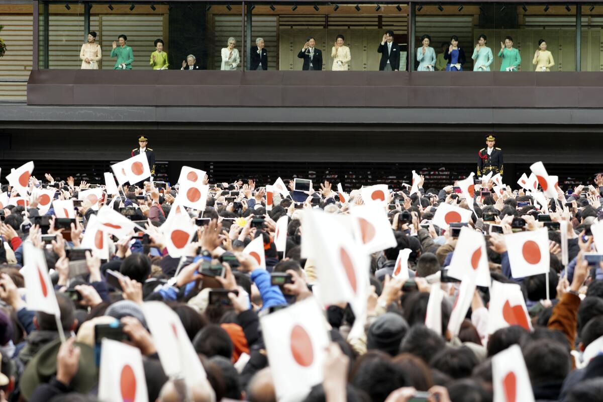 Japan's Emperor Naruhito waves with Empress Masako from a balcony before a large crowd