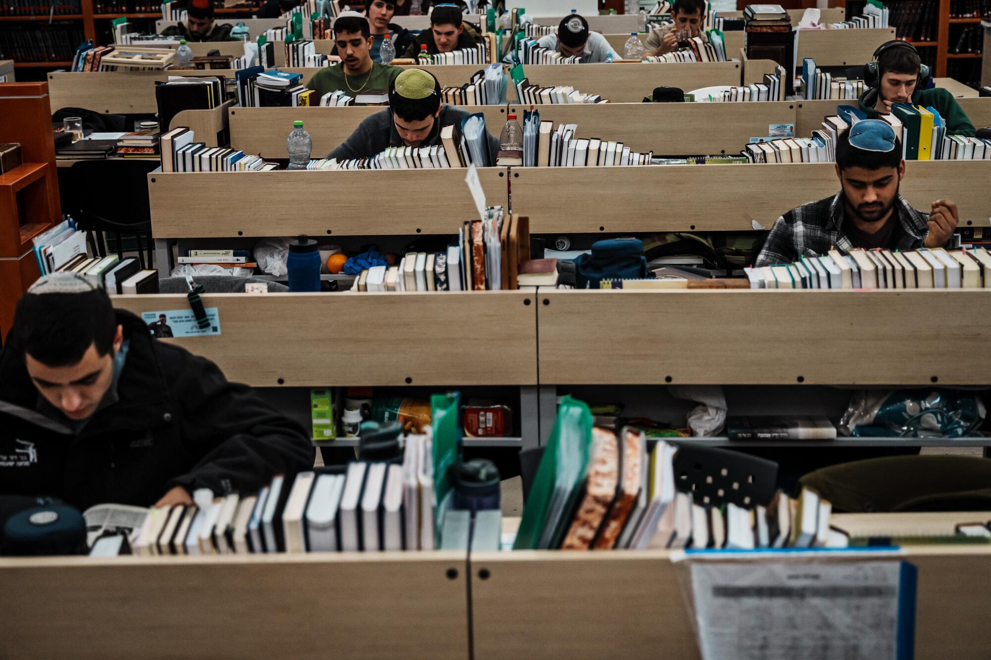 Young men in yarmulkes study at row after row of book-filled desks.