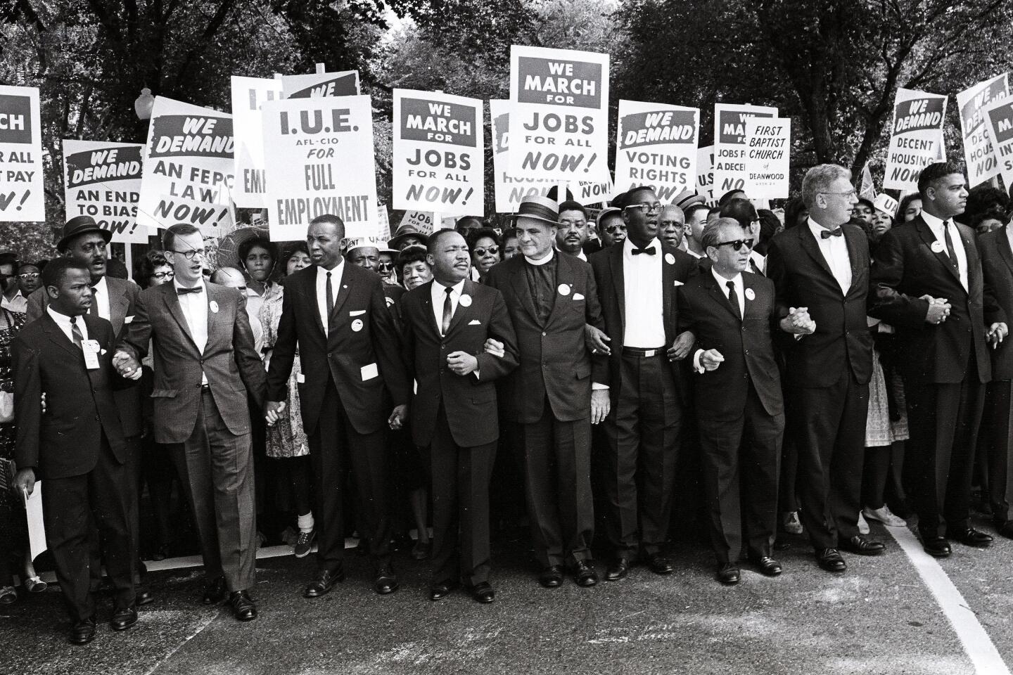 Civil rights activists in suits link hands and carry signs during the March on Washington in 1963