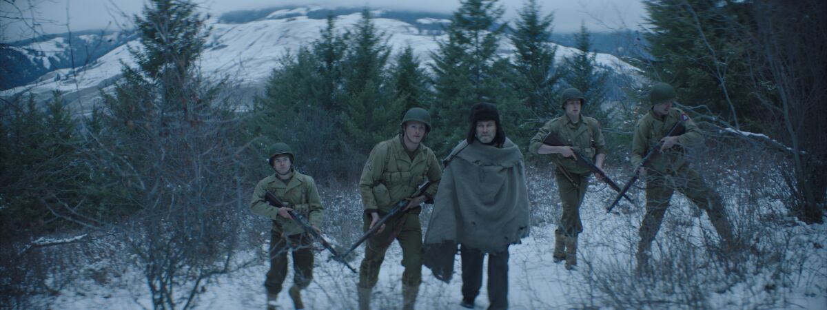 Soldiers carrying guns walk among trees and snow in the Italian mountains.