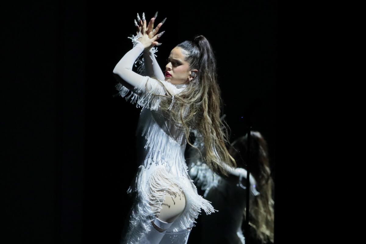 A woman in a white fringed bodysuit, dancing and singing onstage