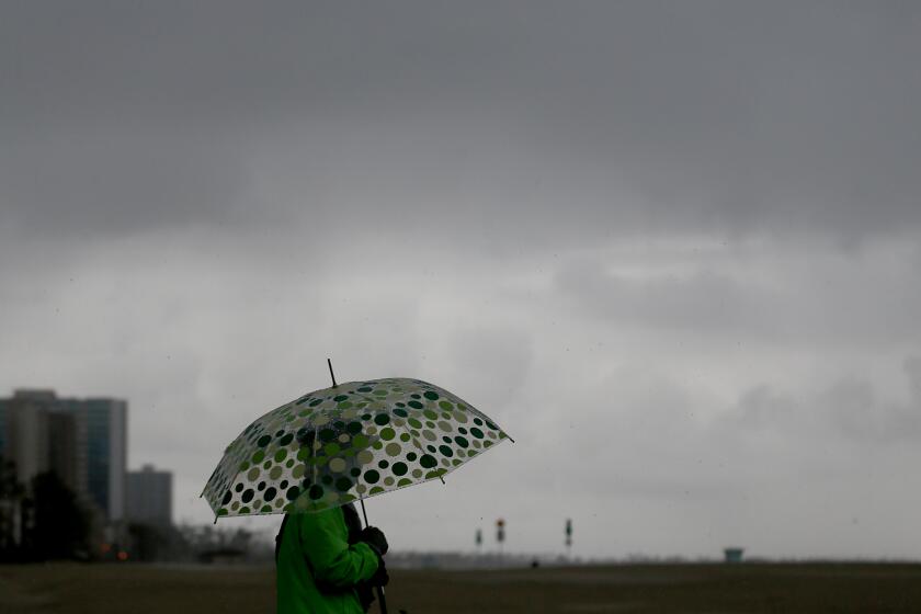 LONG BEACH, CA. - DEC. 28, 2020. A beachgoer strolls in Alamitos Beach in Long Beach on a rainy Monday, Dec. 28, 2020. A regional stay-at-home order in effect across Southern California due to surging COVID-19 hospitalizations was formally extended by California Gov. Gavin Newsom, continuing a ban on all gatherings of people from different households and strict capacity limits at many businesses. T (Luis Sinco/Los Angeles Times)